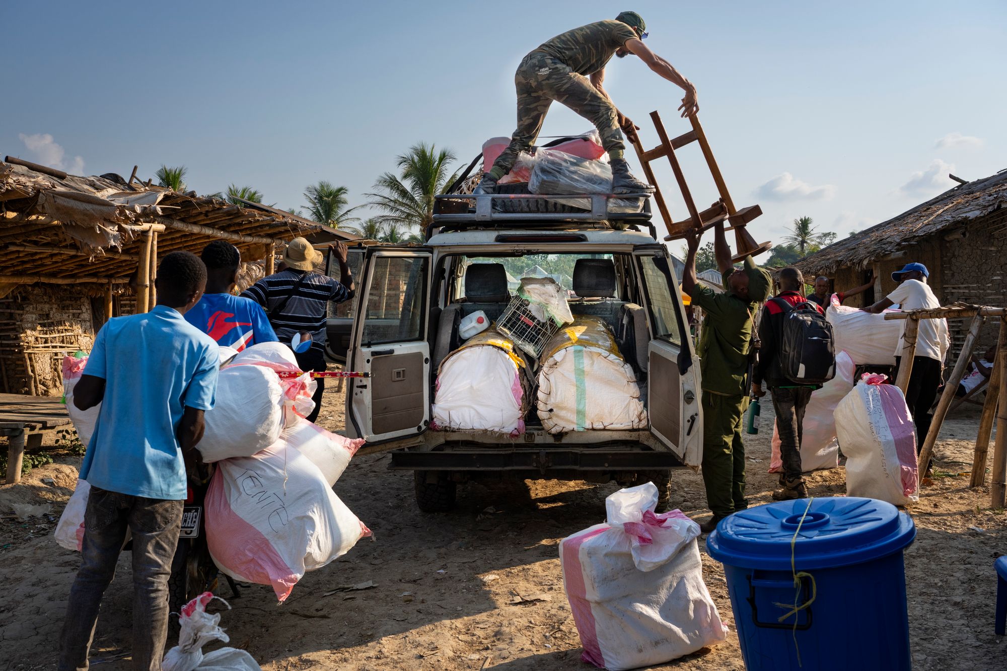 People loading white bags into open back of van on dirt road